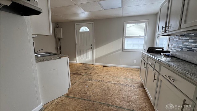 kitchen featuring a sink, a drop ceiling, baseboards, and backsplash