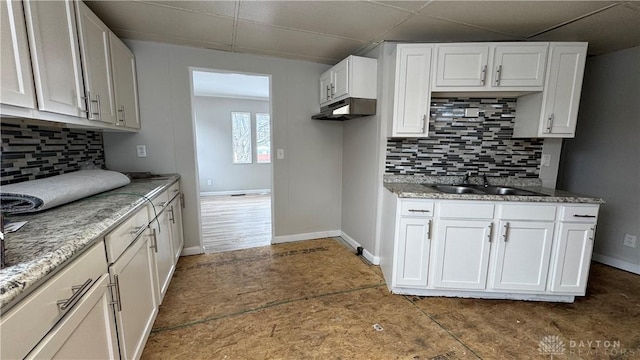 kitchen featuring a sink, backsplash, white cabinetry, baseboards, and a paneled ceiling