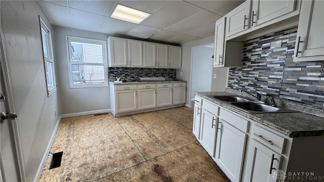 kitchen with a sink, a drop ceiling, tasteful backsplash, white cabinets, and baseboards