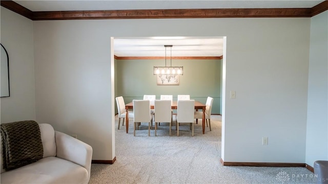 carpeted dining area with a chandelier, baseboards, and ornamental molding