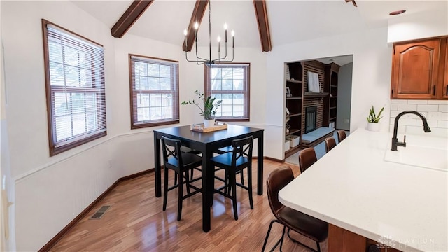 dining room featuring visible vents, vaulted ceiling with beams, a chandelier, light wood-type flooring, and a glass covered fireplace