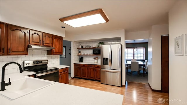 kitchen with under cabinet range hood, open shelves, a sink, appliances with stainless steel finishes, and light countertops