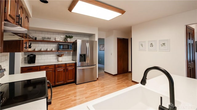 kitchen featuring a sink, decorative backsplash, light countertops, stainless steel appliances, and light wood-type flooring