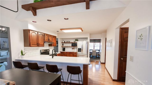 kitchen featuring backsplash, open shelves, appliances with stainless steel finishes, a peninsula, and a sink