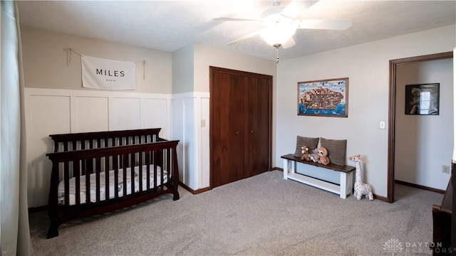 bedroom featuring carpet, wainscoting, a closet, a decorative wall, and a ceiling fan