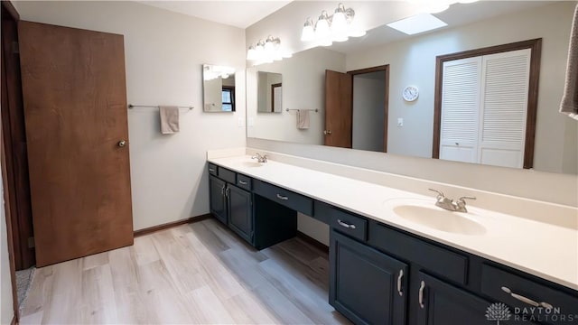 full bathroom featuring double vanity, wood finished floors, baseboards, and a sink