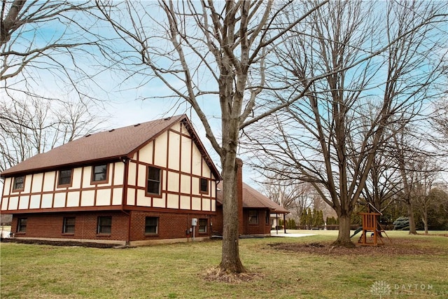 rear view of property with a shingled roof, a lawn, brick siding, and stucco siding