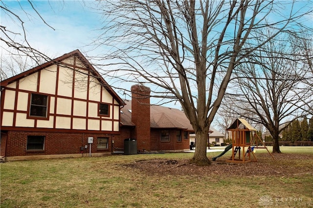 back of house featuring stucco siding, a playground, a yard, brick siding, and a chimney