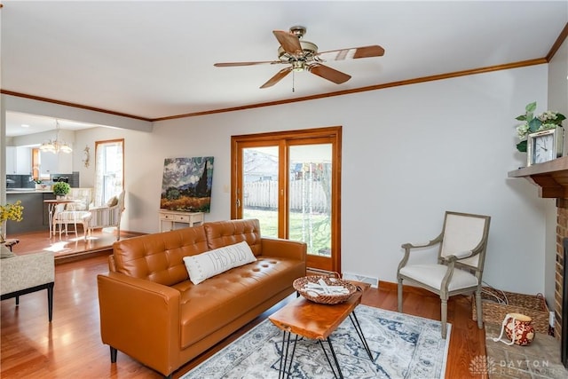 living room with a healthy amount of sunlight, a brick fireplace, ornamental molding, and wood finished floors