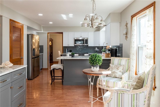 kitchen with gray cabinets, decorative backsplash, light countertops, appliances with stainless steel finishes, and light wood-type flooring