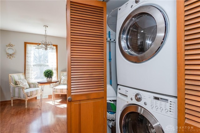 laundry area with a notable chandelier, stacked washer and dryer, wood finished floors, and laundry area