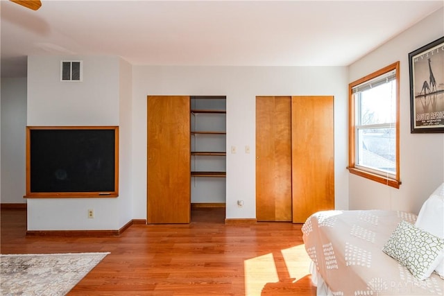 bedroom with visible vents, wood finished floors, multiple closets, and baseboards