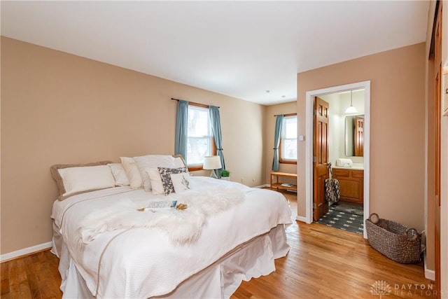 bedroom with ensuite bathroom, light wood-type flooring, and baseboards