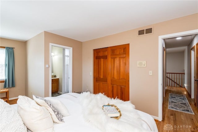 bedroom with visible vents, wood finished floors, connected bathroom, a closet, and baseboards