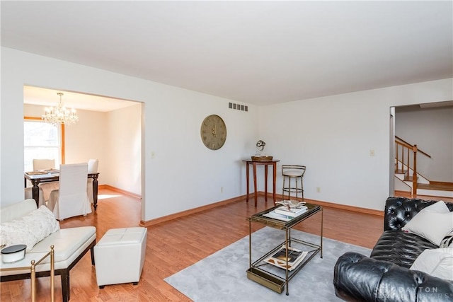 living area featuring visible vents, baseboards, an inviting chandelier, stairs, and light wood-style floors