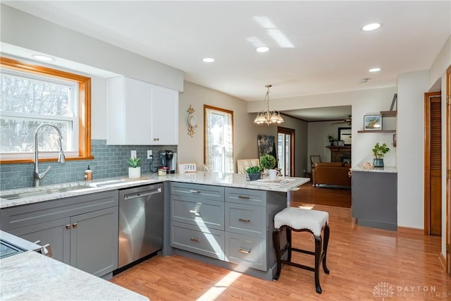 kitchen with gray cabinets, a peninsula, a fireplace, stainless steel dishwasher, and a sink