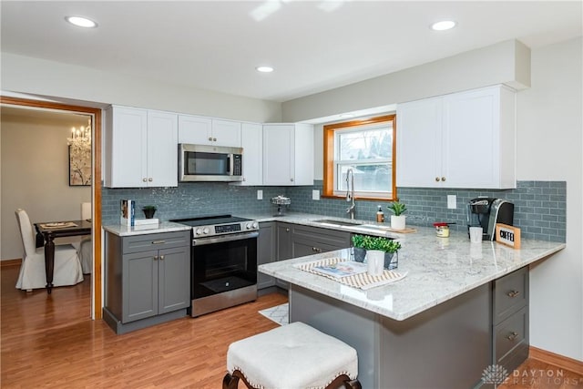 kitchen with appliances with stainless steel finishes, a peninsula, gray cabinetry, and a sink