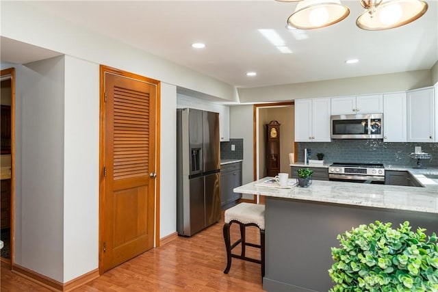 kitchen with light wood-type flooring, tasteful backsplash, appliances with stainless steel finishes, white cabinets, and light stone countertops