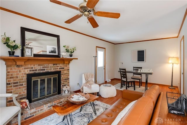 living area with ornamental molding, a brick fireplace, baseboards, and wood finished floors