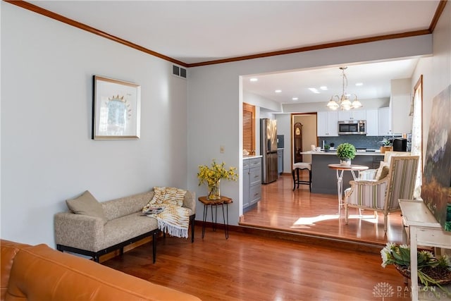 living area with visible vents, crown molding, baseboards, an inviting chandelier, and wood finished floors