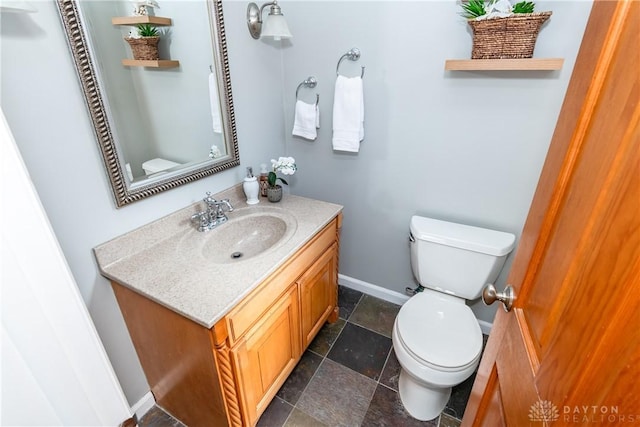 bathroom featuring baseboards, toilet, stone tile flooring, and vanity