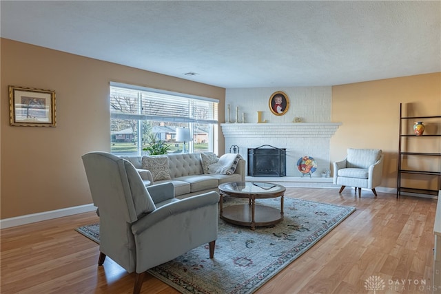 living area with a textured ceiling, a fireplace, light wood-type flooring, and baseboards