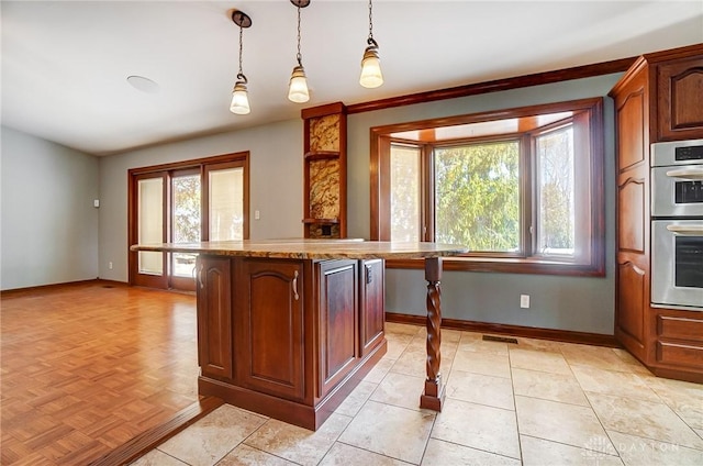 kitchen featuring a center island, baseboards, light stone countertops, double oven, and hanging light fixtures