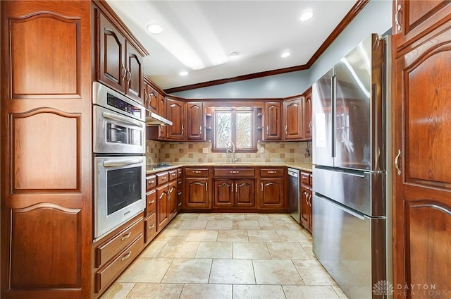 kitchen featuring backsplash, lofted ceiling, ornamental molding, stainless steel appliances, and a sink