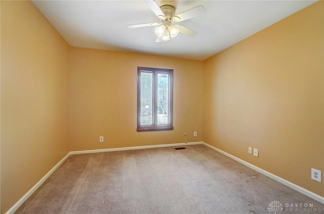 carpeted spare room with visible vents, a ceiling fan, and baseboards