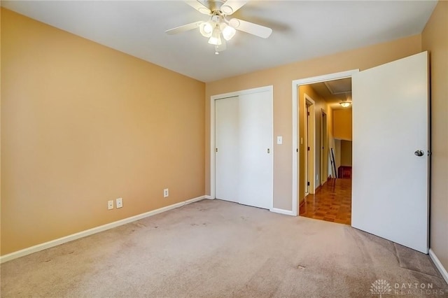 unfurnished bedroom featuring baseboards, carpet floors, attic access, ceiling fan, and a closet