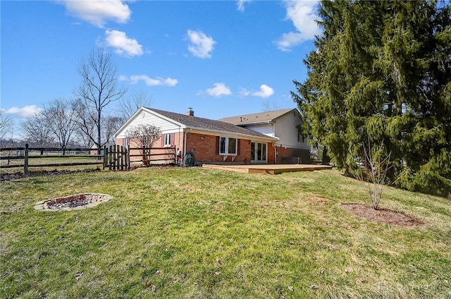 rear view of property featuring brick siding, a lawn, a deck, and fence