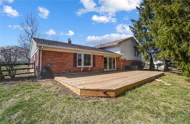 rear view of property featuring fence, a wooden deck, french doors, a lawn, and brick siding