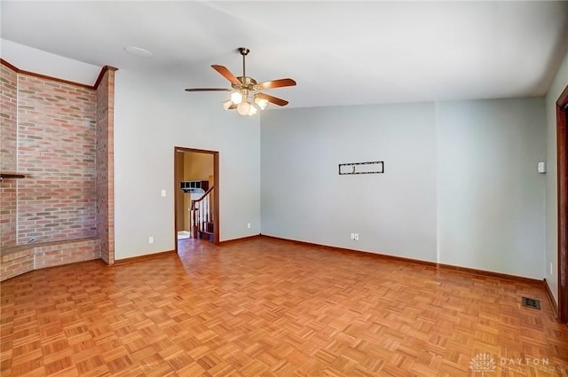 unfurnished room with visible vents, stairway, brick wall, baseboards, and ceiling fan