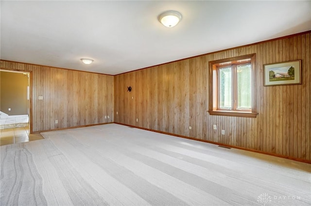 spare room with light carpet, visible vents, wood walls, and baseboards