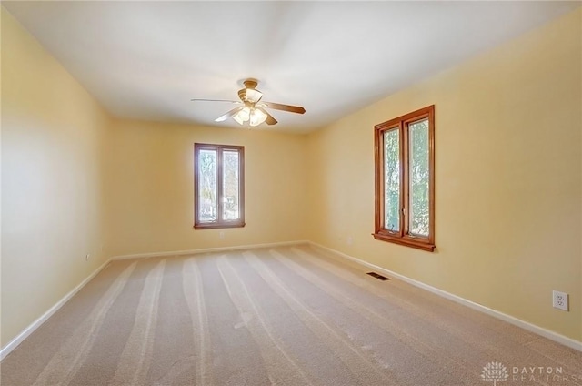 carpeted empty room with visible vents, a ceiling fan, and baseboards