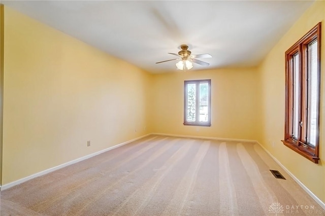 spare room featuring light carpet, visible vents, a ceiling fan, and baseboards