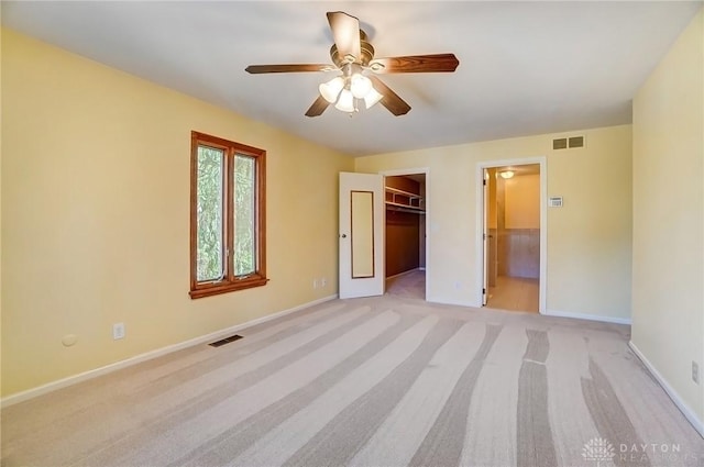 unfurnished bedroom featuring a walk in closet, light colored carpet, visible vents, and baseboards