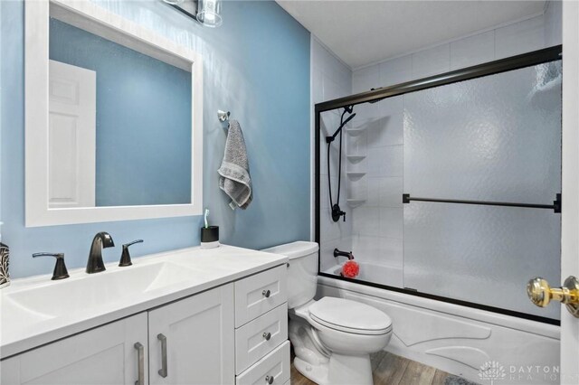 full bathroom with bath / shower combo with glass door, wood finished floors, vanity, and toilet