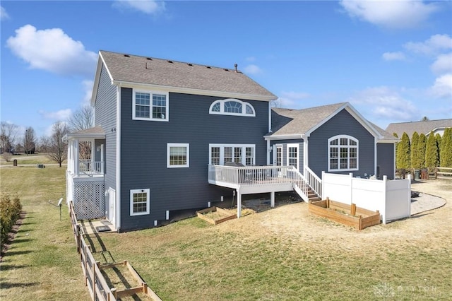 back of property featuring a lawn, fence, a shingled roof, a garden, and a wooden deck