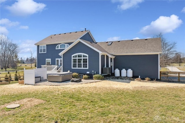 back of house featuring a lawn, cooling unit, a hot tub, and roof with shingles