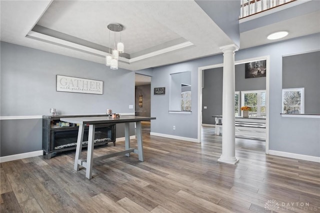 home office with a raised ceiling, wood finished floors, baseboards, and ornate columns