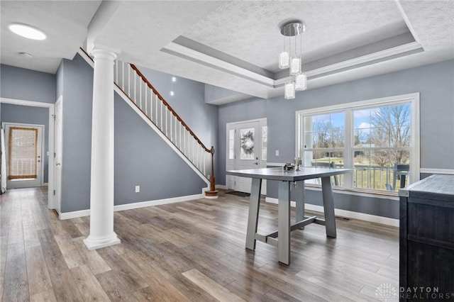 dining space featuring a tray ceiling, decorative columns, wood finished floors, and baseboards