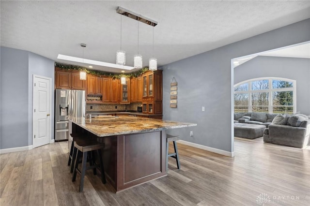 kitchen featuring brown cabinets, light wood-style flooring, a kitchen breakfast bar, backsplash, and stainless steel fridge