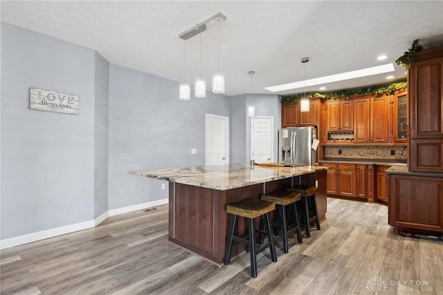 kitchen featuring a kitchen bar, stainless steel fridge, light wood finished floors, baseboards, and light stone countertops