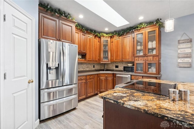 kitchen with decorative light fixtures, appliances with stainless steel finishes, a skylight, light wood-style floors, and brown cabinetry