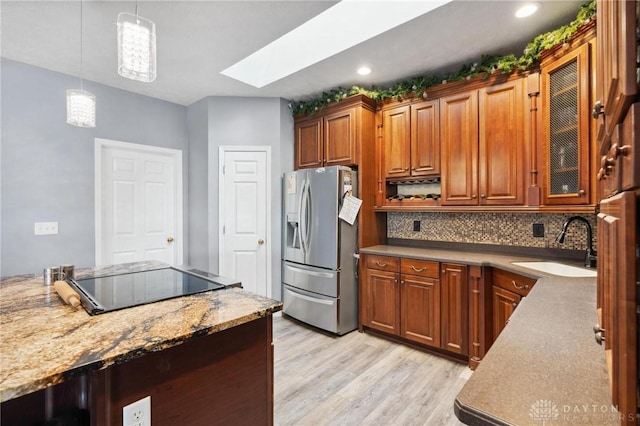 kitchen featuring a skylight, a sink, stainless steel fridge, black electric stovetop, and light wood-type flooring