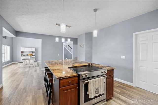 kitchen with stainless steel electric range oven, light stone counters, a center island with sink, baseboards, and light wood-style floors