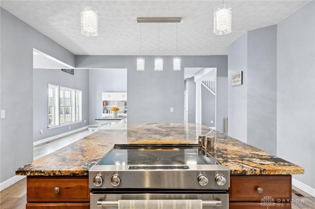 kitchen featuring stone counters, stainless steel electric stove, open floor plan, and brown cabinetry