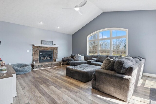 living area with baseboards, light wood finished floors, ceiling fan, a stone fireplace, and vaulted ceiling