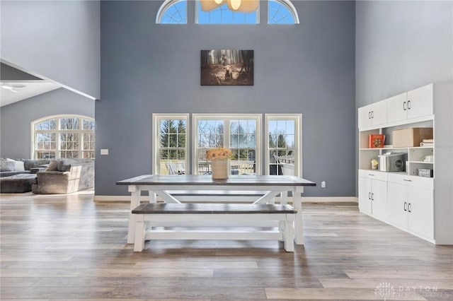 dining space with baseboards, light wood-type flooring, and a towering ceiling